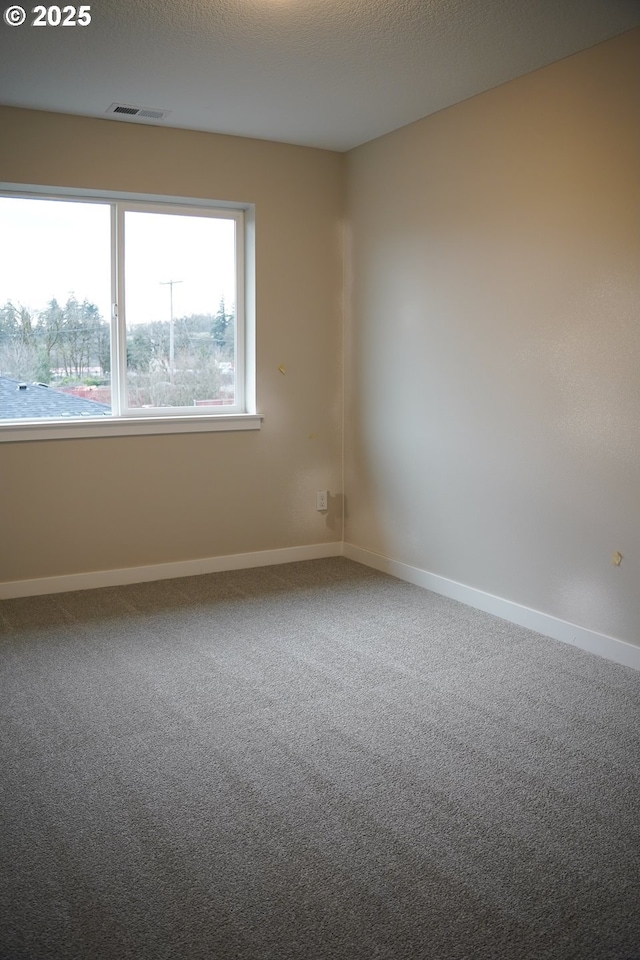 carpeted empty room featuring a textured ceiling, visible vents, and baseboards