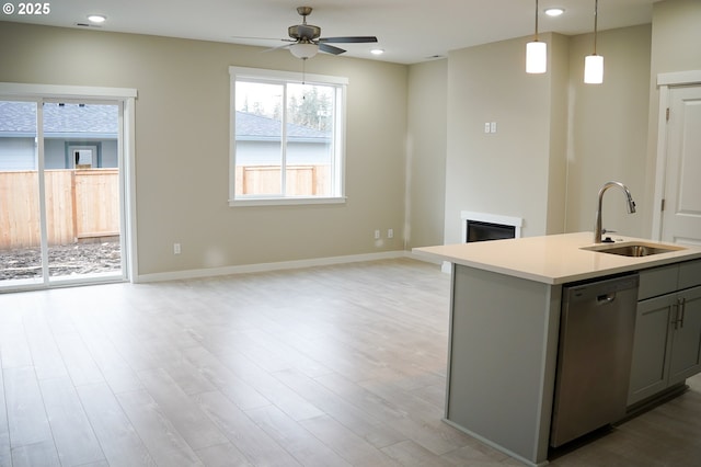 kitchen with gray cabinets, light countertops, stainless steel dishwasher, open floor plan, and a sink