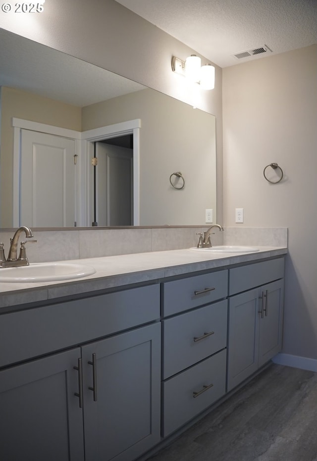 bathroom with wood finished floors, visible vents, a sink, and double vanity