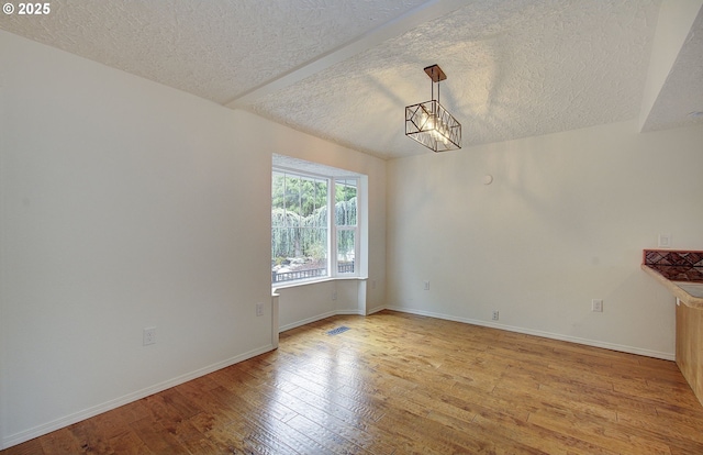 empty room with a textured ceiling, light wood-style flooring, baseboards, and a chandelier