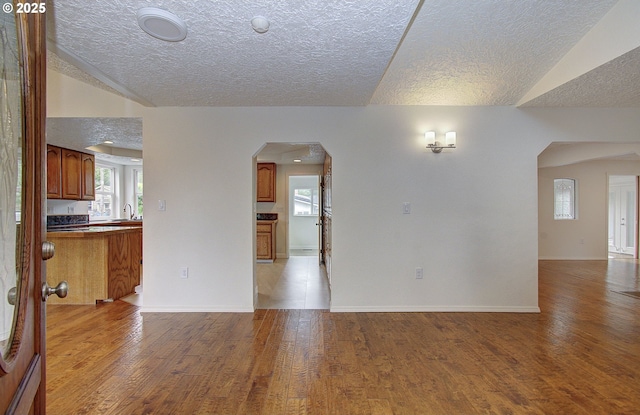 unfurnished living room featuring wood finished floors, a textured ceiling, a sink, and arched walkways