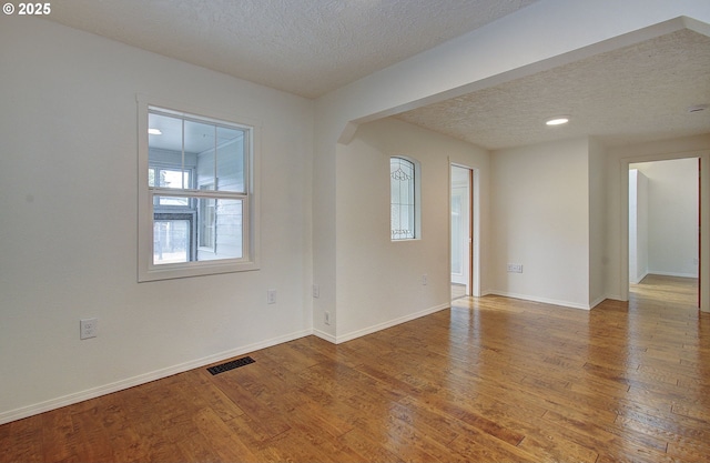 unfurnished room with a textured ceiling, wood finished floors, baseboards, and arched walkways