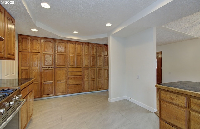kitchen featuring brown cabinetry, a textured ceiling, recessed lighting, baseboards, and stainless steel gas range oven