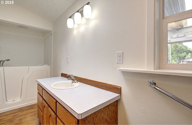 full bath featuring a textured ceiling, vaulted ceiling, a garden tub, wood finished floors, and vanity
