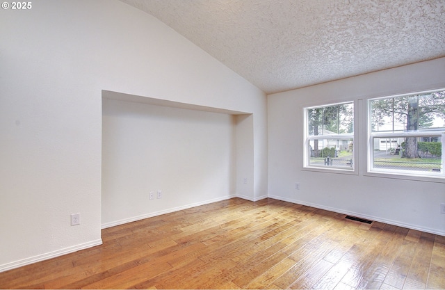 empty room featuring vaulted ceiling, light wood finished floors, a textured ceiling, and baseboards
