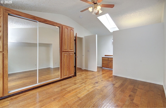 bonus room featuring a skylight, lofted ceiling, ceiling fan, light wood-style flooring, and a textured ceiling