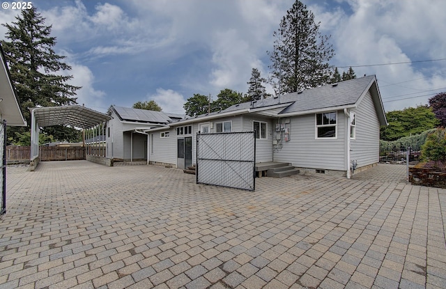 back of property with fence, roof mounted solar panels, a carport, and entry steps