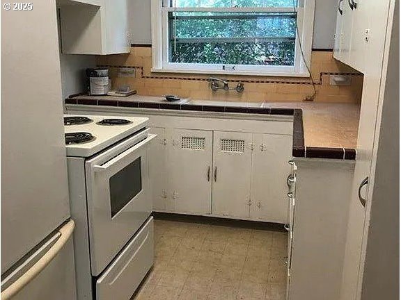 kitchen featuring white cabinetry, tile countertops, fridge, white electric stove, and backsplash