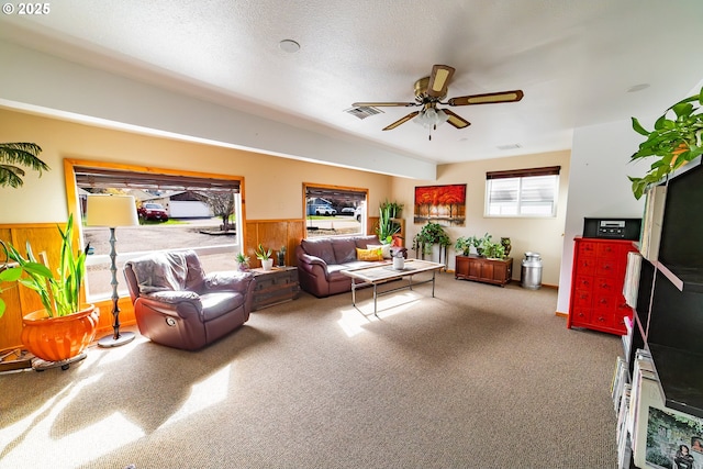 living room with ceiling fan, wooden walls, and a textured ceiling