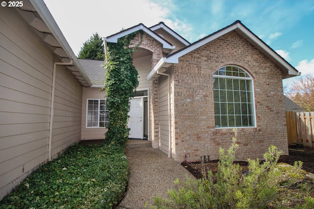 doorway to property with fence, brick siding, and roof with shingles