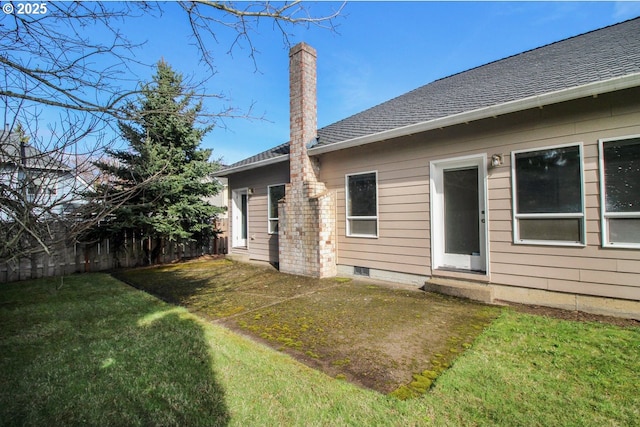 rear view of house with a lawn, a shingled roof, a chimney, and fence