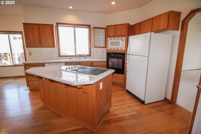 kitchen featuring light wood-type flooring, brown cabinets, a kitchen island, tile countertops, and white appliances