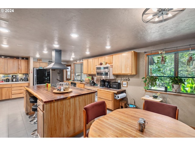 kitchen with fridge, butcher block countertops, stainless steel oven, island exhaust hood, and a kitchen island