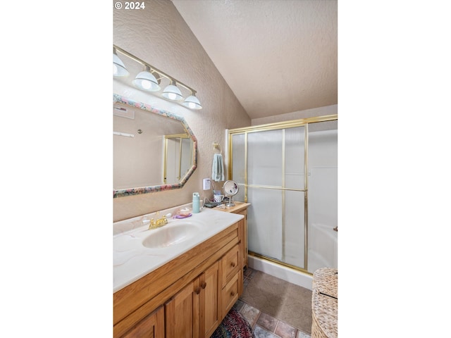 bathroom with vanity, a textured wall, vaulted ceiling, and a shower stall