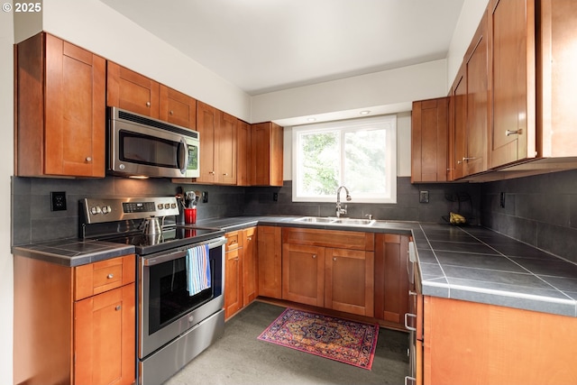 kitchen featuring appliances with stainless steel finishes, a sink, tile countertops, brown cabinets, and tasteful backsplash