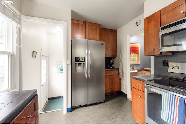 kitchen featuring appliances with stainless steel finishes, brown cabinetry, tile counters, and baseboards