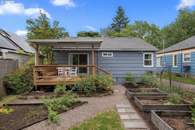 rear view of property featuring a vegetable garden, a wooden deck, roof with shingles, and fence