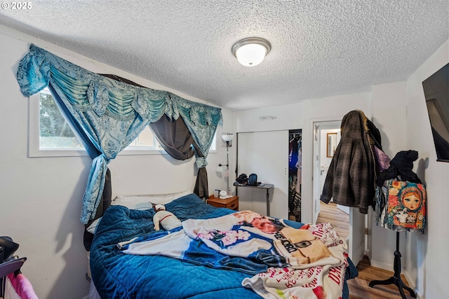 bedroom with a textured ceiling, wood finished floors, and a closet