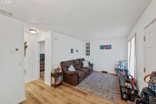 living area featuring a textured ceiling, wood finished floors, and baseboards