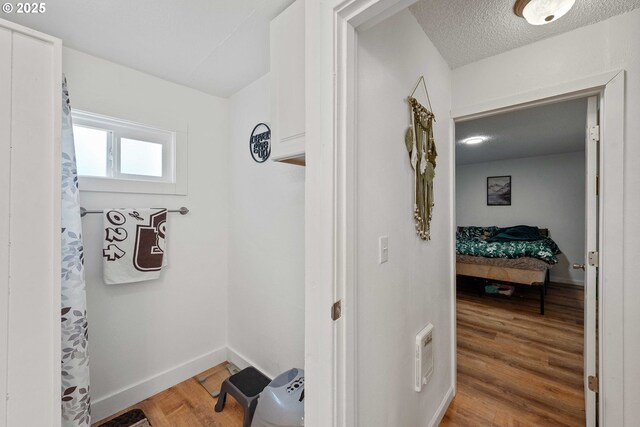 corridor featuring wood finished floors, a textured ceiling, and baseboards