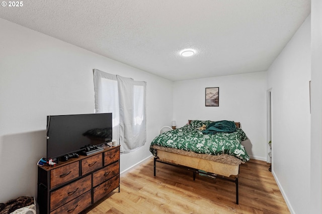 bedroom featuring light wood-style flooring, a textured ceiling, and baseboards