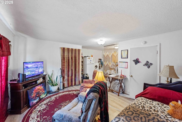 bedroom with a textured ceiling, wood finished floors, and freestanding refrigerator