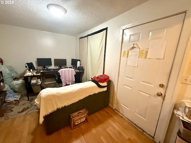 bedroom featuring light wood-type flooring, a textured ceiling, and an office area
