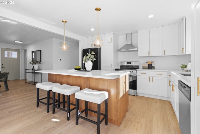 kitchen featuring white cabinets, stainless steel appliances, a kitchen island, and wall chimney range hood