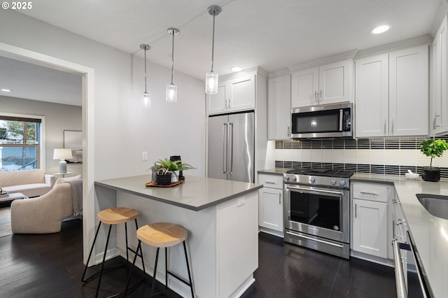 kitchen with pendant lighting, white cabinetry, stainless steel appliances, a kitchen breakfast bar, and dark hardwood / wood-style flooring