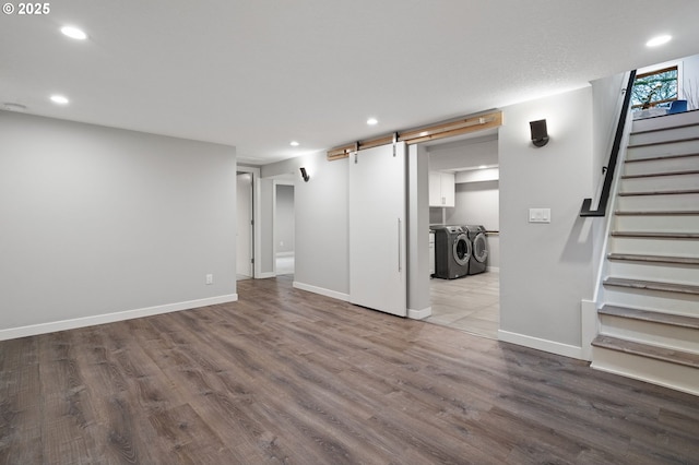 basement featuring wood-type flooring, a barn door, and washing machine and clothes dryer