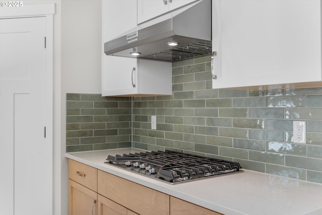 kitchen featuring under cabinet range hood, stainless steel gas cooktop, white cabinets, light countertops, and backsplash