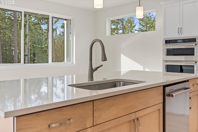 kitchen with hanging light fixtures, stainless steel appliances, a sink, and light countertops