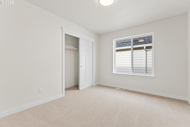 unfurnished bedroom featuring light carpet, visible vents, baseboards, a textured ceiling, and a closet