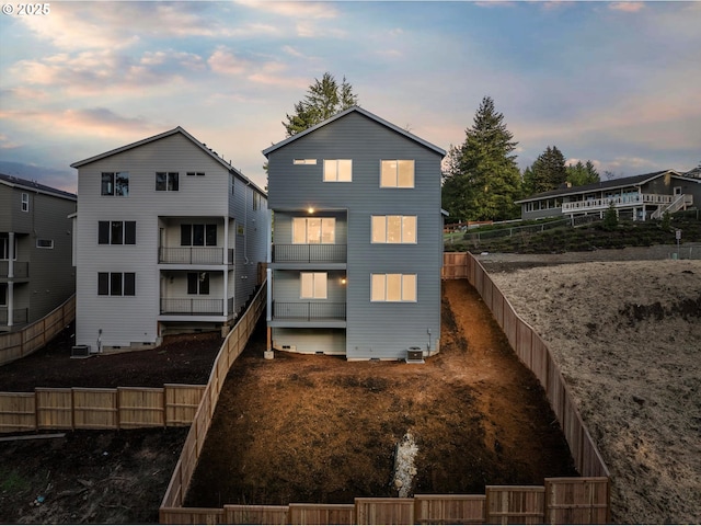 back of property at dusk with a fenced backyard and central AC unit