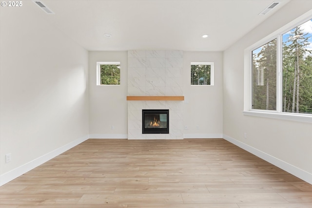 unfurnished living room with plenty of natural light, visible vents, a tiled fireplace, and light wood finished floors