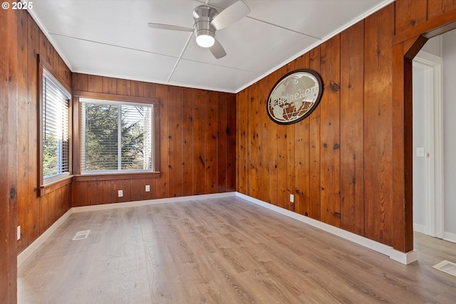 unfurnished room with ceiling fan, ornamental molding, wooden walls, and light hardwood / wood-style floors