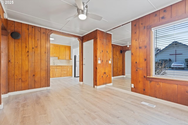 unfurnished room featuring ceiling fan, a healthy amount of sunlight, light hardwood / wood-style floors, and wood walls