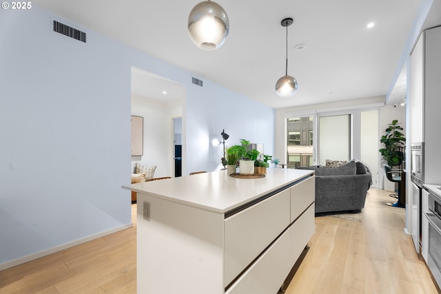 kitchen with white cabinets, hanging light fixtures, light wood-type flooring, and a center island