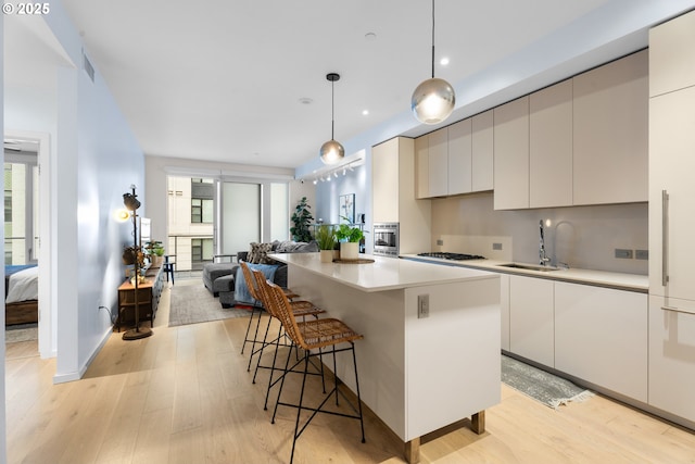 kitchen with sink, stainless steel gas cooktop, light hardwood / wood-style floors, a kitchen island, and pendant lighting