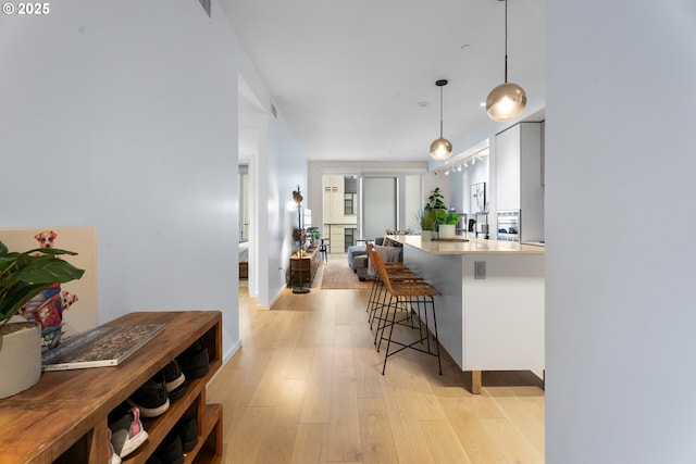 kitchen with white cabinets, light hardwood / wood-style floors, pendant lighting, and a kitchen bar