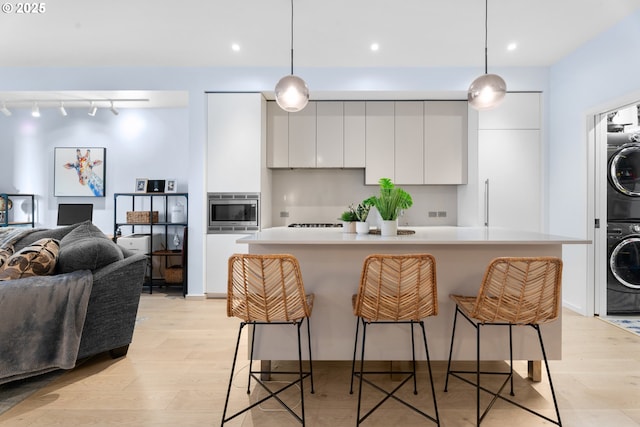 kitchen featuring stacked washer and clothes dryer, decorative light fixtures, white cabinets, and a kitchen island