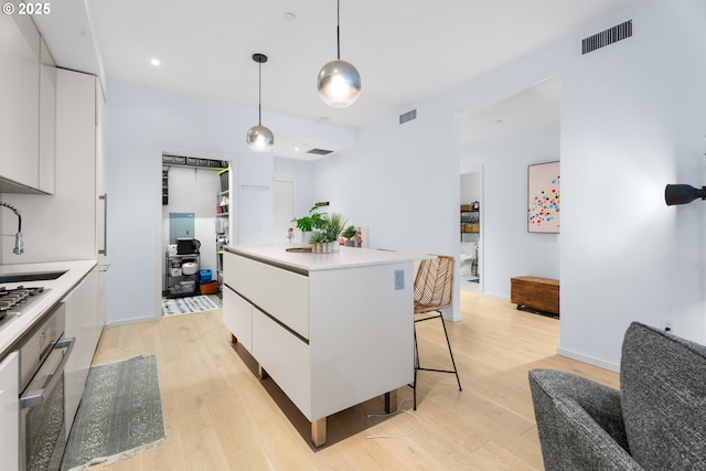 kitchen with hanging light fixtures, a center island, stainless steel appliances, light wood-type flooring, and white cabinets