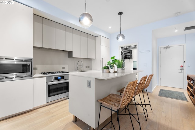 kitchen with white cabinets, stainless steel appliances, a kitchen island, sink, and decorative light fixtures