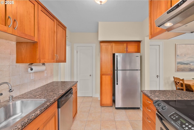 kitchen featuring appliances with stainless steel finishes, a sink, brown cabinetry, and decorative backsplash