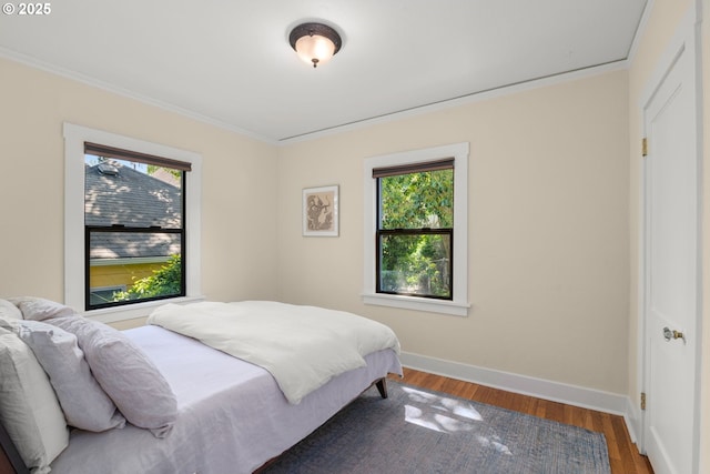 bedroom featuring multiple windows, ornamental molding, baseboards, and wood finished floors