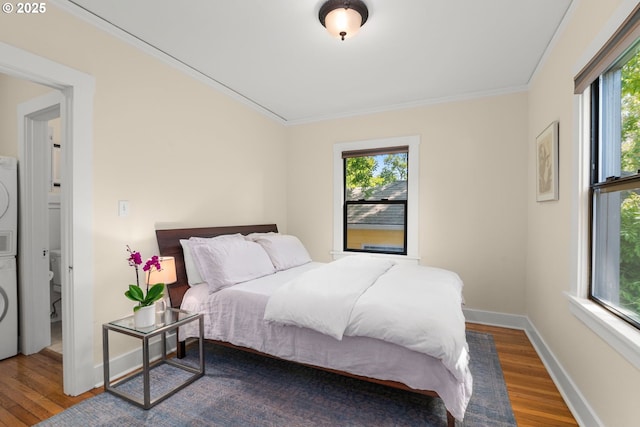 bedroom featuring stacked washer / drying machine, wood finished floors, multiple windows, crown molding, and baseboards