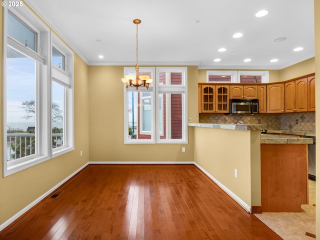 kitchen with crown molding, hanging light fixtures, light hardwood / wood-style floors, decorative backsplash, and kitchen peninsula