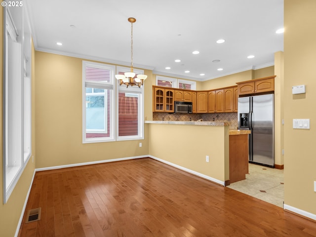 kitchen featuring crown molding, light wood-type flooring, kitchen peninsula, stainless steel appliances, and decorative backsplash