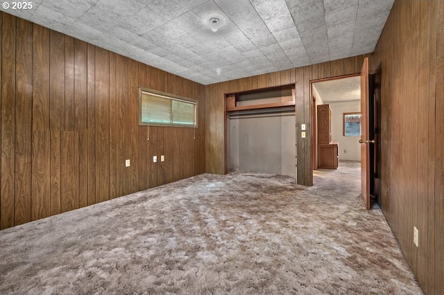 unfurnished bedroom with a closet, carpet, and wooden walls