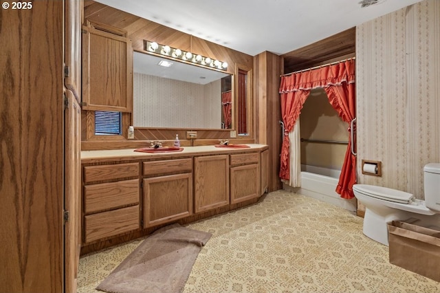 bathroom with double vanity, a sink, toilet, and wallpapered walls